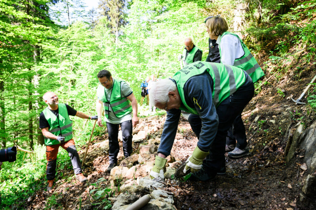 Der Deutsche Alpenverein bessert Wanderwege aus, und Bundespräsident Steinmeier legt selbst Hand an, um einen Weg auszubessern, der durch einen umgekippten Baum beschädigt wurde. Foto: Bundesregierung/Steins